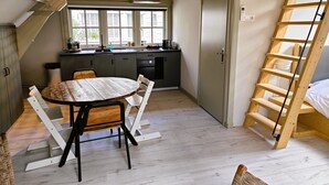 Una cuina petita amb zona de menjador, una escala de fusta i vista a l'exterior.