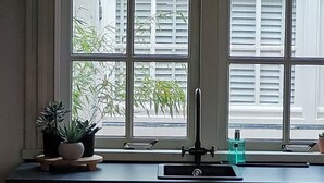 Cuina amb finestra, un rentapeus i dues plantes en testos sobre el taulell.