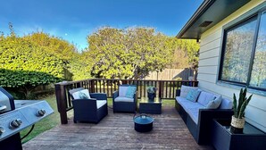 Une terrasse dotée de mobilier d’extérieur, d’un barbecue et d’une grande fenêtre donnant sur un jardin.
