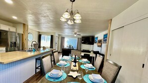 Un coin repas avec une table en bois dressée pour quatre personnes, une cuisine équipée d’appareils électroménagers modernes et un ventilateur de plafond.