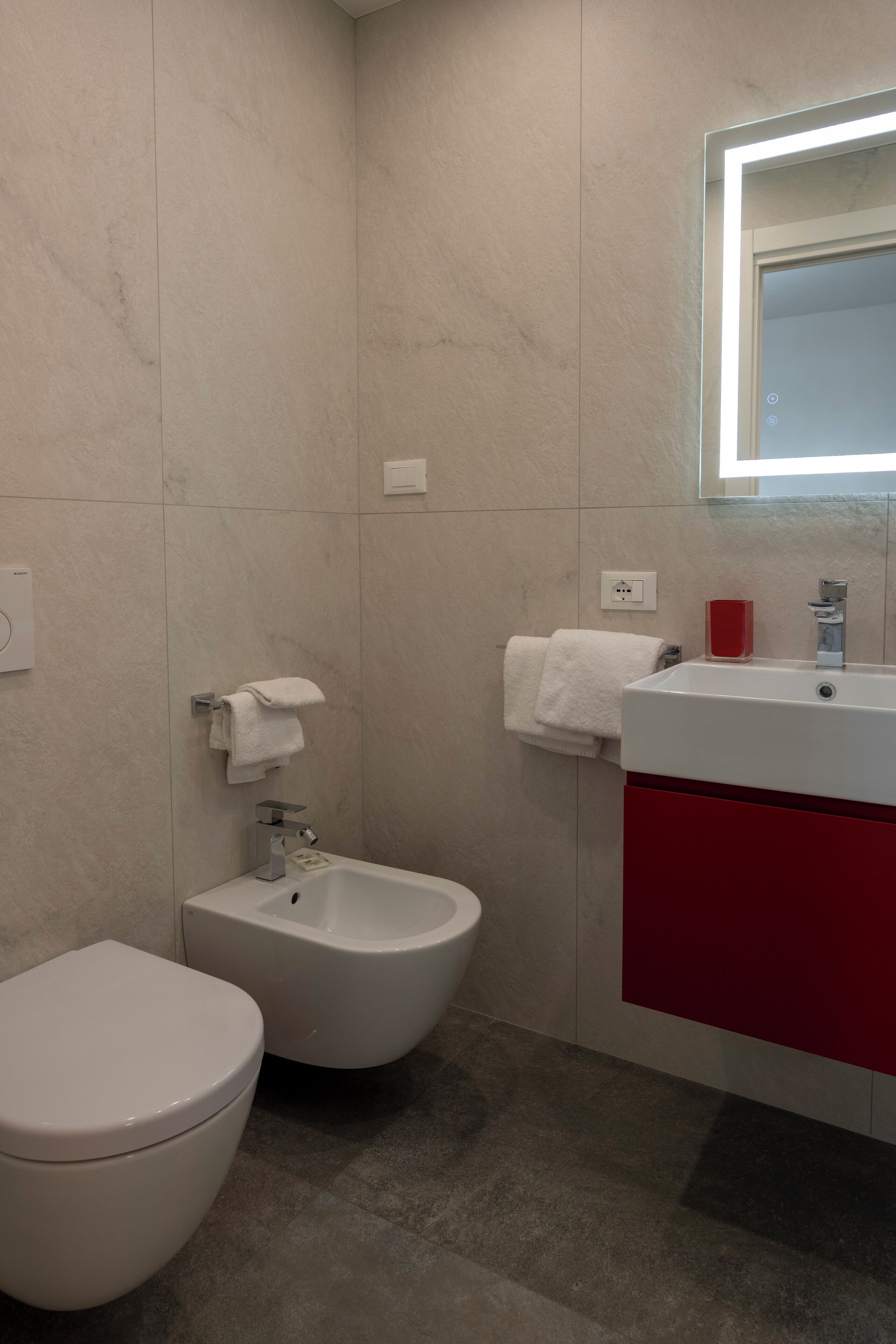 A bathroom with a toilet, bidet, and a sink with a red cabinet.