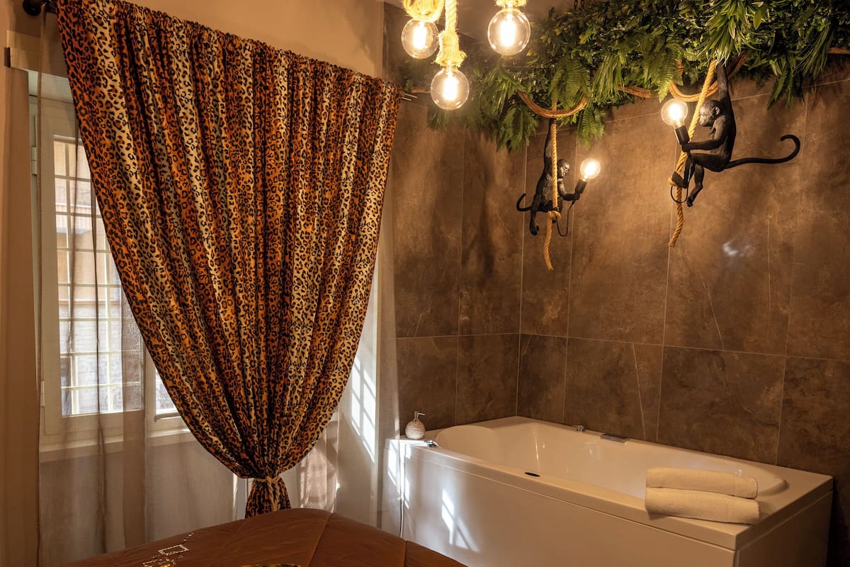 A bedroom with a large bed, a bathtub, and a window with curtains.