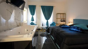 A modern bedroom with a large bed, a separate bathroom with a bathtub, and a small round table with a bottle. - Jacuzzi Rooms Vatican Museum (Rome)