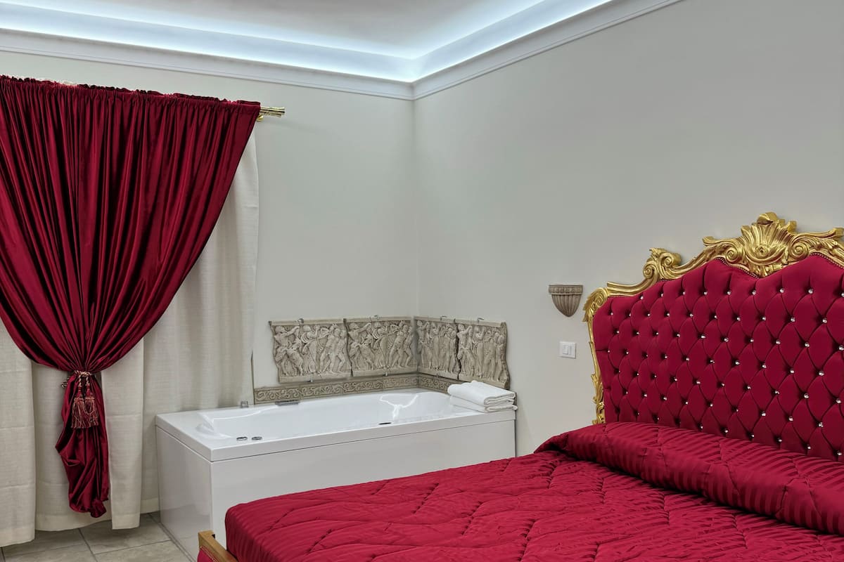A bedroom with a large bed, a white bathtub, and a red curtain.