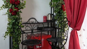 A room with a metal-framed table and two chairs, a red box, a kettle, and a red curtain. - Jacuzzi Rooms Vatican Museum (Rome)