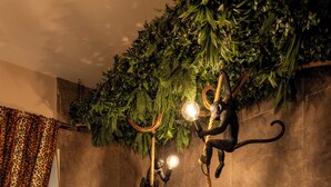 A modern bathroom with a large bathtub, a shower, and a decorative wall with green foliage and a monkey sculpture. - Jacuzzi Rooms Vatican Museum (Rome)