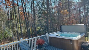 Une terrasse dotée d’un jacuzzi, de mobilier d’extérieur et offrant une vue sur une forêt.