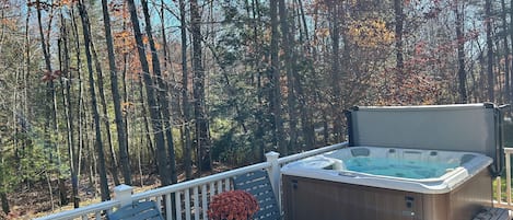 A deck with a hot tub, outdoor furniture, and a view of a forest.