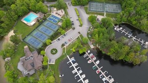 Vue aérienne d’un espace de loisirs comprenant une piscine, des courts de tennis et un port de plaisance.