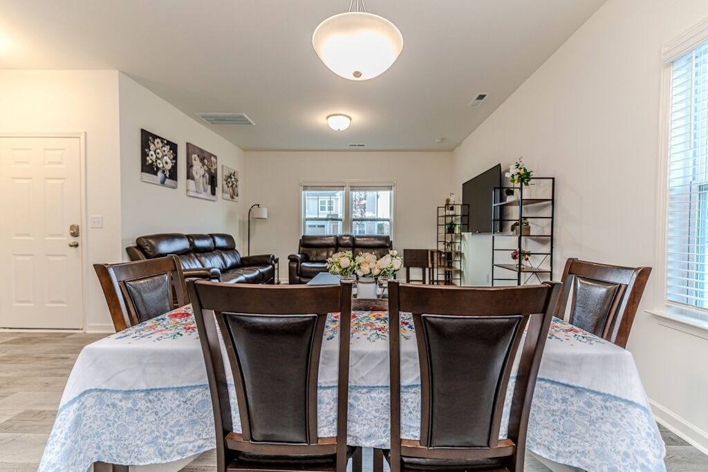 A dining area with a round table, six chairs, and a chandelier.
