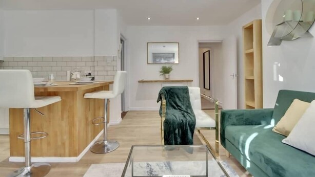 Ein moderner Wohnraum mit Küchenzeile, einem Esstisch mit Barhocker, einem grünen Sofa und einem Glastisch.