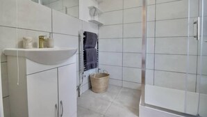 Ein modernes Badezimmer mit weißen Fliesen, einem Waschbecken, einem Spiegel und einer Duschkabine.