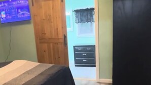 Ein Schlafzimmer mit Bett, einer Holztür, einem Schminktisch und einem an der Wand befestigten Fernseher.