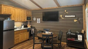 A kitchen with wooden cabinets, a refrigerator, a microwave, a stove, and a dining area with a table and chairs. - Modern luxury- Rustic Charm (Afton)