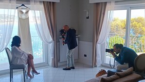 A room with a large window, a chandelier, a sofa, and a chair. - Relais Tiaré Bed and Breakfast (Bacoli)
