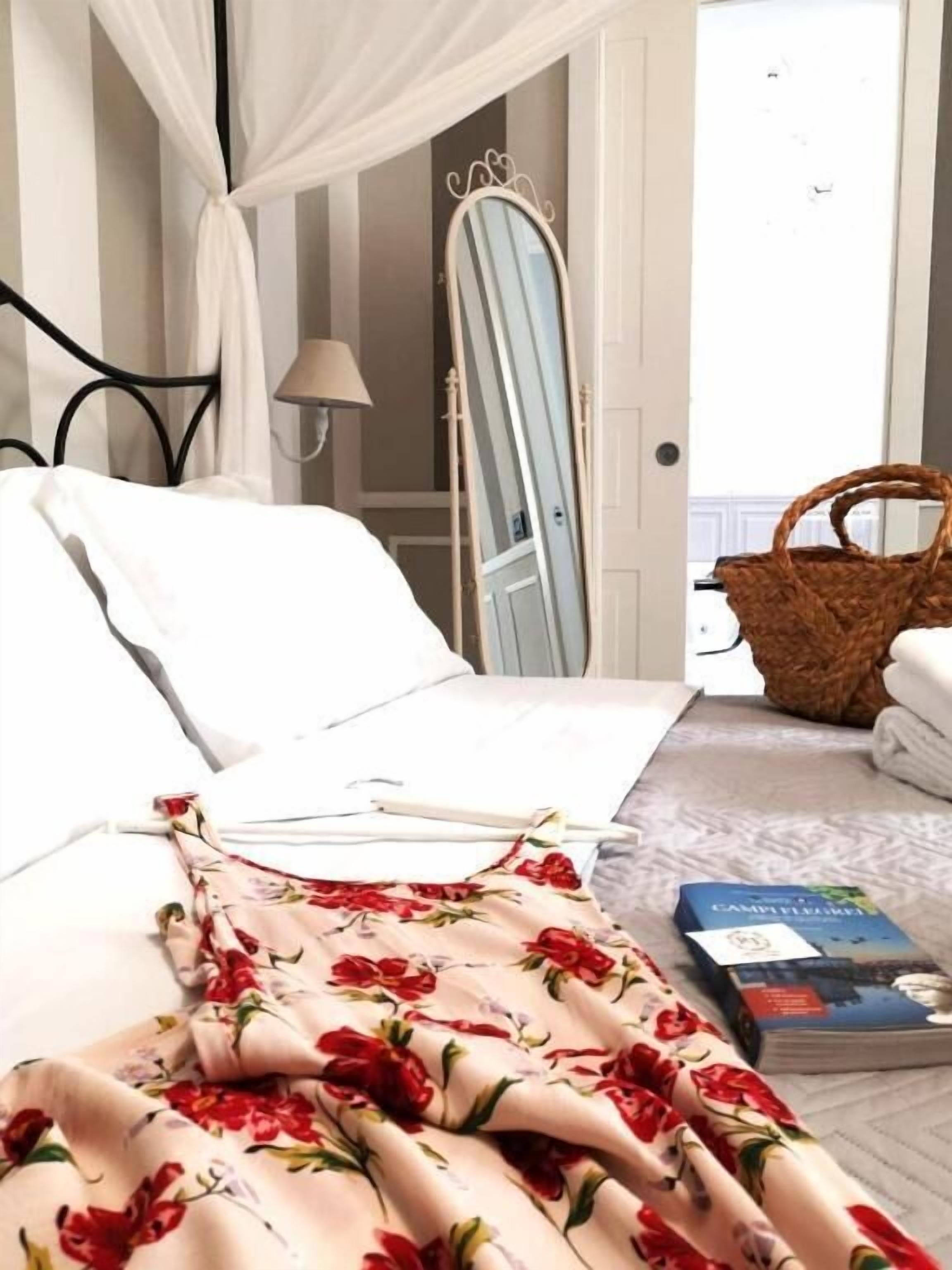 Ein Bett mit einer decke mit floralem Muster, eine Nachttischlampe, ein Spiegel, ein Korbwesen und ein Buch auf dem Boden.