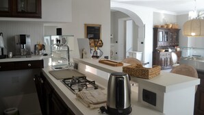 A modern kitchen with a gas stove, kettle, and various appliances. There is a white countertop with a coffee machine and a chalkboard menu. The kitchen has a rustic feel with wooden cabinets and a large window. - Relais Tiaré Bed and Breakfast (Bacoli)