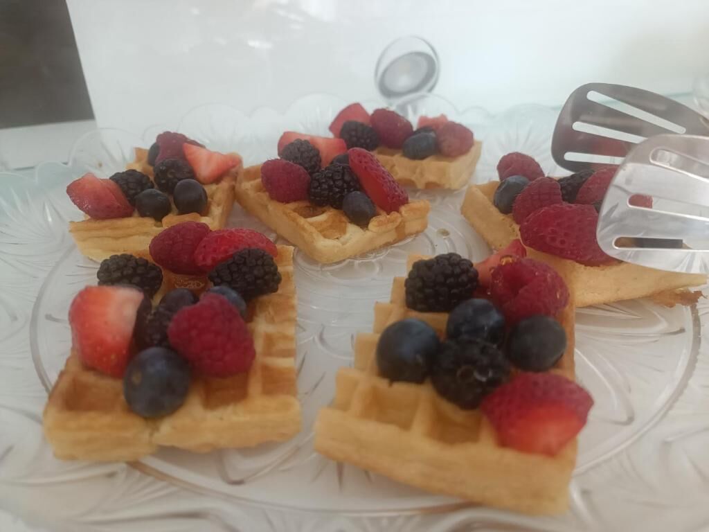 A clear glass plate with waffles topped with strawberries, raspberries, and blueberries.