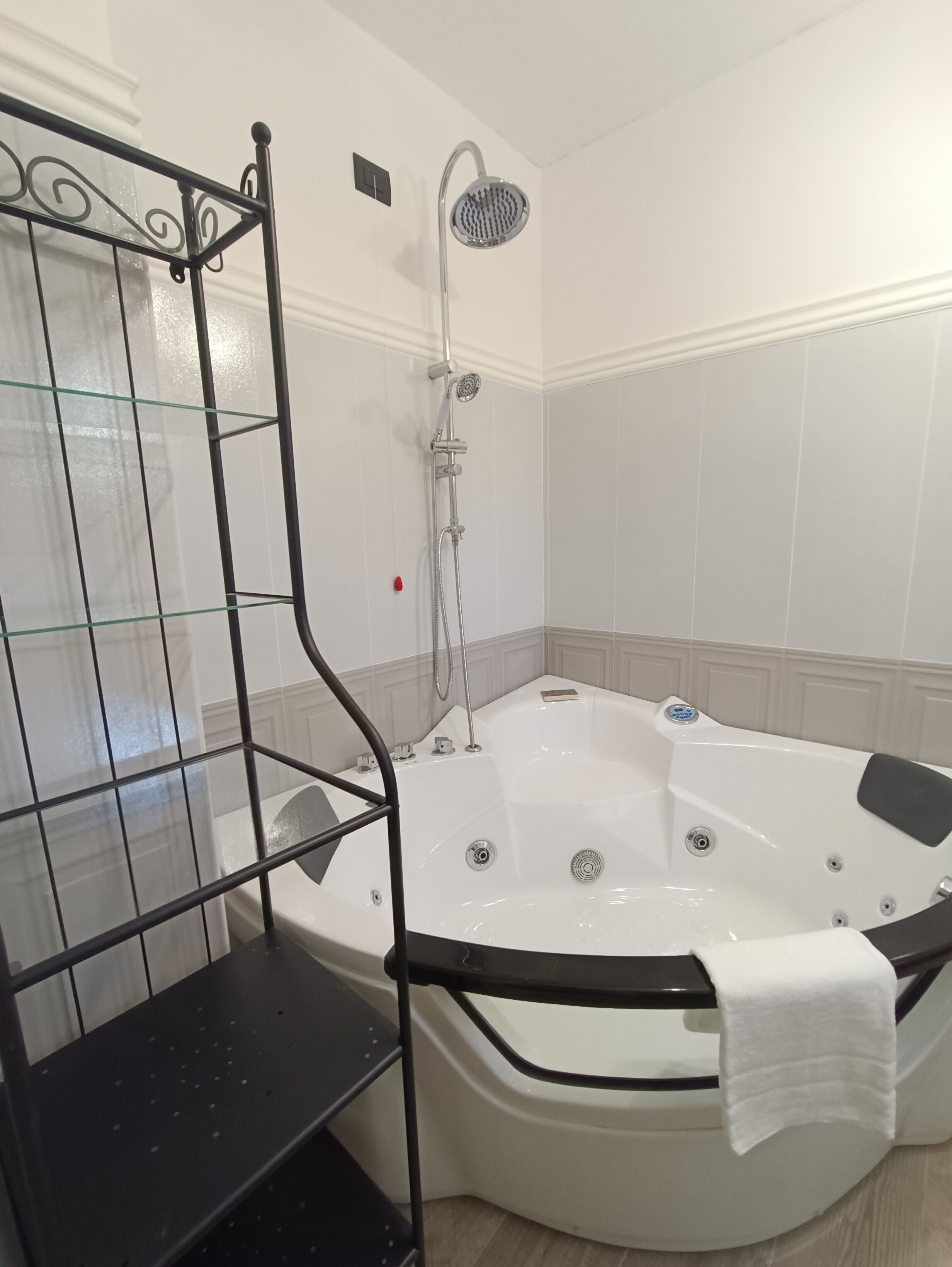 A bathroom with a glass shower enclosure, a bathtub, and a black metal shelf.