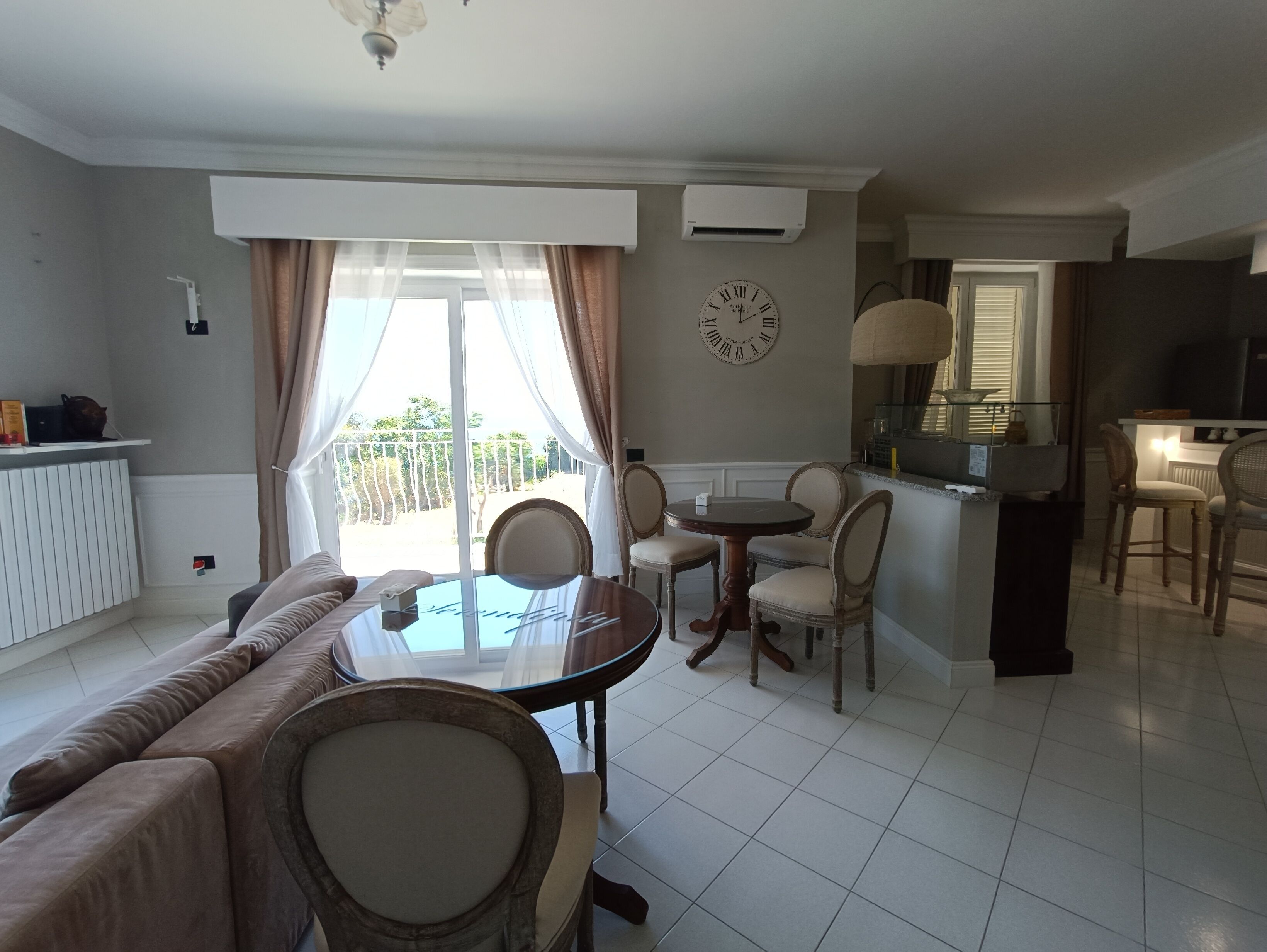 Una sala de estar con sofá, una mesa de comedor con sillas, una zona de cocina y un balcón con cortinas.