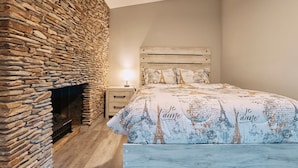A bedroom with a stone fireplace, a bed with Eiffel Tower-themed bedding, and a nightstand with a lamp. - Sedona Retreat:HotTub View Trail (Sedona)