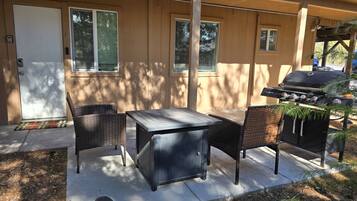 Une terrasse avec une table et des chaises, un barbecue et un espace abrité avec une porte.