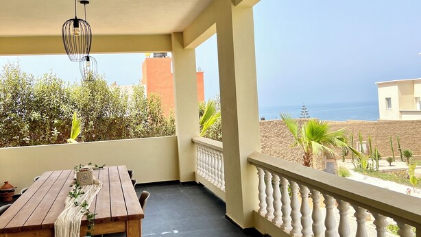 Ein Balkon mit Holztisch, einer Pendelleuchte und Blick aufs Meer.