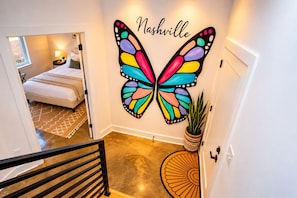 A hotel room with a bed, a nightstand, a lamp, and a wall with a colorful butterfly decoration.