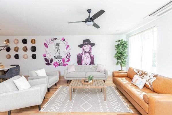 Ein modernes Wohnzimmer mit einem grauen Sofa, einem braunen Ledersofa, einem Couchtisch und einer Wand mit dekorativen Hüten und einem Wandgemälde.