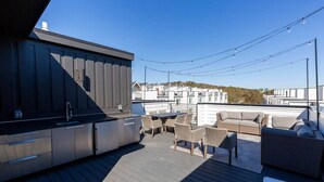 Una terrazza esterna con angolo bar, mobili in vimini e vista sugli edifici circostanti.