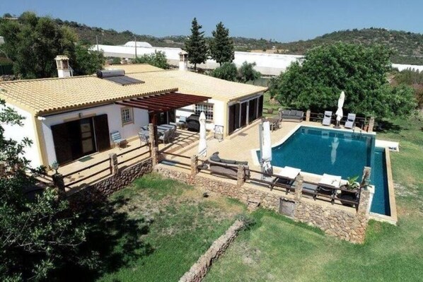A house with a swimming pool, a patio with outdoor furniture, and a view of the surrounding landscape.