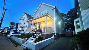 Une maison à deux étages avec un porche, un numéro « 167 » bien visible et une voiture garée devant.