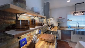 Une cuisine moderne avec un dosseret en pierre, des étagères en bois et un four encastré.
