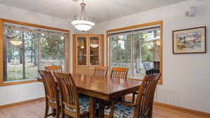 A dining area with a wooden table and chairs, large windows, a chandelier, and a bookshelf. - Spacious Sunriver retreat w/hot tub + bikes.  Family + Pet Friendly! (Sunriver)
