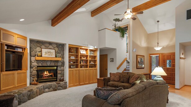 A spacious living room with a fireplace, wooden shelves, a comfortable couch, and a staircase leading to another level. - Spacious Sunriver retreat w/hot tub + bikes.  Family + Pet Friendly! (Sunriver)