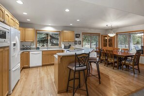 A modern kitchen with wooden cabinets, a central island, bar stools, and a dining table with chairs.