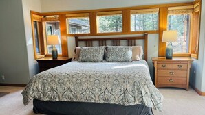 A bedroom with a large bed, wooden headboard, two nightstands, a dresser, and large windows with a view of trees. - Spacious Sunriver retreat w/hot tub + bikes.  Family + Pet Friendly! (Sunriver)