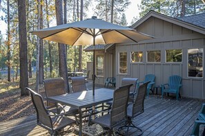 A wooden deck with a table and chairs, an umbrella, and a building with windows.