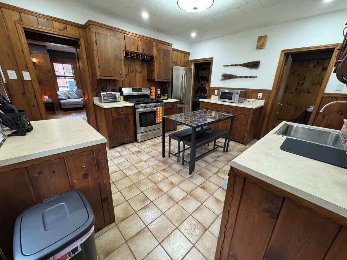 Una cocina con armarios de madera, una isla central, un refrigerador y un microondas.