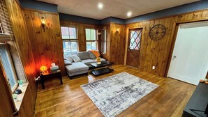 Un salon chaleureux avec des murs en bois, un canapé gris, une table basse et un tapis.