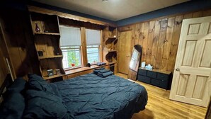 Une chambre avec un grand lit, des murs en bois, une fenêtre et une porte.
