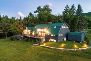 Een groot, twee verdiepingen tellend huis met een groen dak, een overdekte veranda en een kleine aanleun schuur.