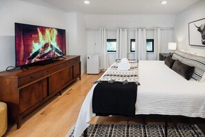 Een slaapkamer met een groot bed, een televisie op een houten kast, en een raam met gordijnen.