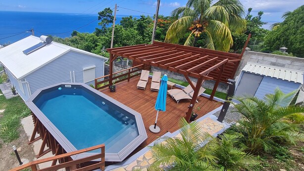 A rooftop pool area with a wooden deck, lounge chairs, and a pergola.