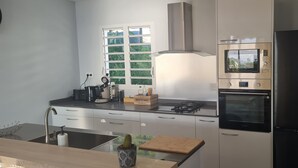A modern kitchen with a stainless steel refrigerator, built-in oven, and microwave. There is a window with a view of greenery outside.