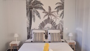 A bedroom with a large bed, a wall-mounted air conditioner, two bedside tables with lamps, and a tropical-themed tapestry.