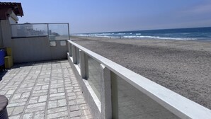 Blick auf einen Strand vom Balkon, mit Betonboden und Geländer, der auf einen Sandstrand und das Meer hinausblickt.