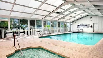 An indoor swimming pool with a glass ceiling, surrounded by a white fence and a poolside area with chairs.