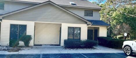 A two-story building with a garage, a covered driveway, and a parked car.