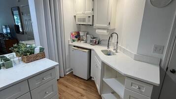 A compact kitchen with white cabinetry, a microwave, a coffee maker, and a sink.